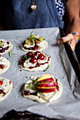 A woman holding a baking tray with unbaked mini pizzas