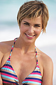 Reife Frau mit kurzen blonden Haaren im Bikini am Strand