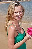 A young blonde woman on a beach wearing a green top and a pink bikini