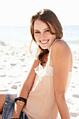 A young brunette woman on a beach wearing a beige top