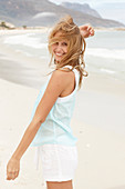 Junge blonde Frau im hellblauen Top und weißer Sommershorts am Strand