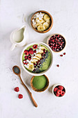 Bowl with healthy smoothie for breakfast in composition with various additives as fruit and matcha powder