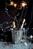 Silvesterparty: Champagnerflaschen in Sektküler dekoriert mit Sterngirlande und Wunderkerzen