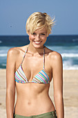 A blonde woman with short hair on a beach wearing a bikini top