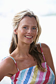 A young blonde woman on a beach wearing a light-blue top