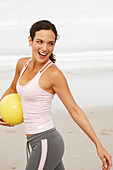 A young brunette woman by the sea wearing sports clothes with a ball