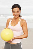A young brunette woman by the sea wearing sports clothes with a ball