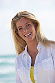 A young blonde woman on a beach wearing a white blouse