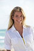 A young blonde woman on a beach wearing a white blouse