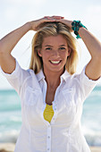 A young blonde woman on a beach wearing a white blouse