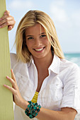 A young blonde woman on a beach wearing a white blouse