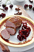 Duck breast with cherries on golden plate