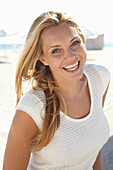 A mature blonde woman on a beach wearing a white top