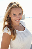 A mature blonde woman on a beach wearing a white top