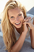 A mature blonde woman lying on a sandy beach wearing a white top