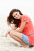 A brunette woman on a beach wearing a salmon-coloured top and a denim skirt