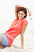 A brunette woman on a beach wearing a salmon-coloured top and a denim skirt