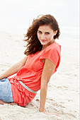 A brunette woman on a beach wearing a salmon-coloured top and a denim skirt