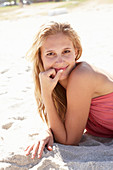 A young blonde woman on a beach wearing a pink top