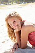 A young blonde woman on a beach wearing a pink top