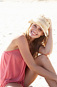 A young blonde woman on a beach wearing a pink top and a beige hat