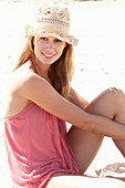 Junge blonde Frau im rosa Top und beigem Hut am Strand