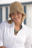 A young blonde woman on a beach wearing a white blouse and a brown hat