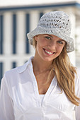 Junge blonde Frau in weißer Bluse und weißem Häkelhut am Strand