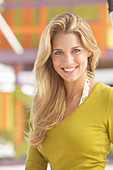 A young blonde woman on a beach wearing an olive top