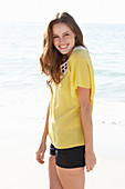 Junge brünette Frau im gelben Sommerkleid und schwarzer Shorts am Strand