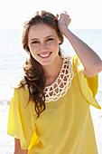 A young brunette woman on a beach wearing a yellow summer dress