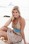 A blonde woman on a beach wearing a beige summer dress