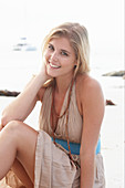 A blonde woman on a beach wearing a beige summer dress