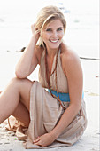 A blonde woman on a beach wearing a beige summer dress