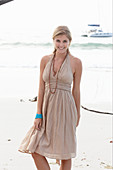 A blonde woman on a beach wearing a beige summer dress