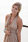 A blonde woman on a beach wearing a beige summer dress