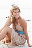 A blonde woman on a beach wearing a beige summer dress