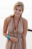 A blonde woman on a beach wearing a beige summer dress