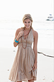 A blonde woman on a beach wearing a beige summer dress