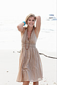 A blonde woman on a beach wearing a beige summer dress