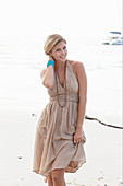 A blonde woman on a beach wearing a beige summer dress