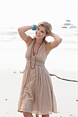 A blonde woman on a beach wearing a beige summer dress