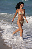 A young brunette woman on a beach wearing a silver bikini
