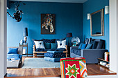 Blaues Wohnzimmer mit verschiedenen Sitzmöbeln, Liege und Kunstwerk an der Wand