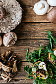 Different kind of mushrooms and ruccola on a wooden background