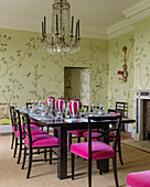 Stühle mit pinkfarbenem Samtbezug um gedeckten Esstisch, darüber französischer Kristallleuchter im Esszimmer mit Chinoiserie-Tapete