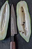 Halved, young papaya with a knife on a black surface