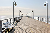 Ocean pier with balustrade, street lamps and benches below blue sky