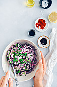 Hands holding a bowl with onion salad with sumac nad parsley on a grey background