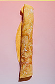 Rolled pancake with powdered sugar on a pink background